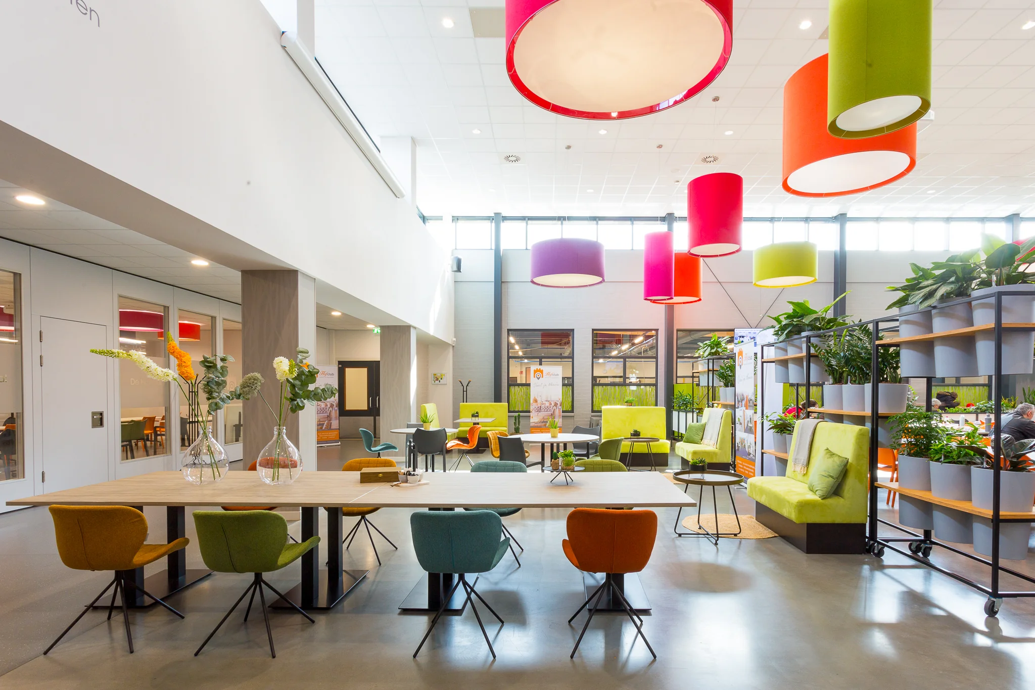 Kleurrijke en modern ingerichte ontmoetingsruimte aan de Niels Bohrweg met planten, designmeubilair en opvallende hanglampen.